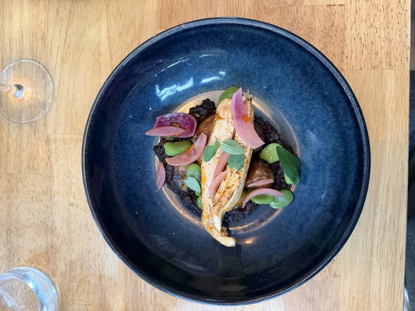A seared fish fillet over black rice with fava beans and pickled onion