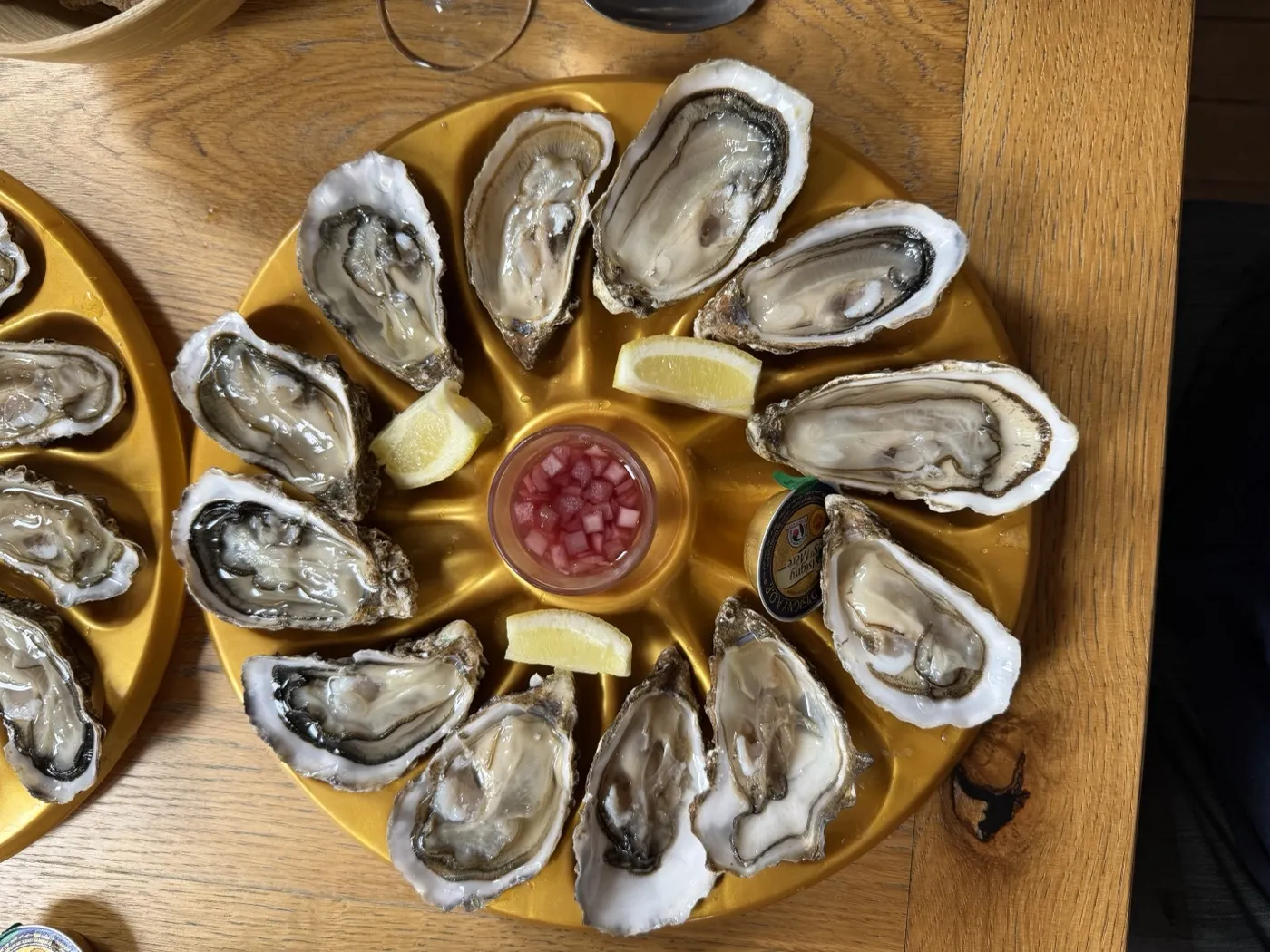 A dozen open oysters on a gold platter with lemon and mignonette